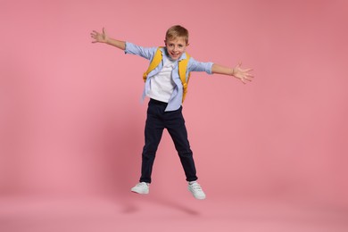 Photo of Happy schoolboy with backpack jumping on pink background