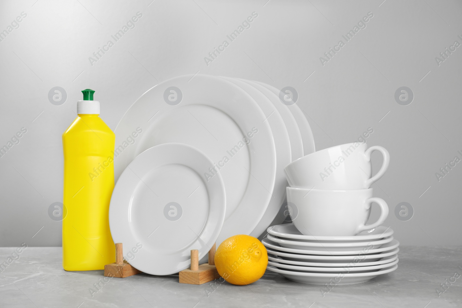 Photo of Set of clean tableware, dish detergent and lemon on grey table against light background