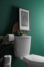 Decor elements, paper rolls and toilet bowl near green wall. Bathroom interior