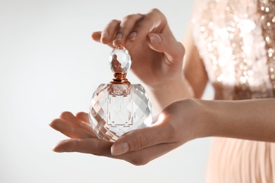 Photo of Young woman with bottle of perfume on light background, closeup