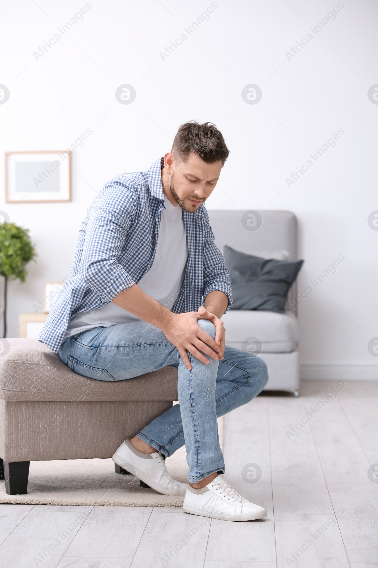 Photo of Young man suffering from knee pain at home