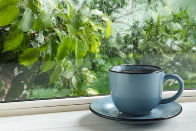 Photo of Cup of hot drink on windowsill, space for text. Rainy weather