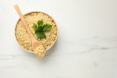 Photo of Delicious bulgur with parsley and spoon on white marble table, top view. Space for text