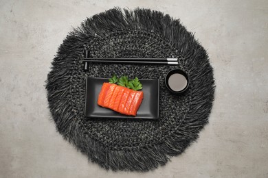 Plate of tasty salmon slices, soy sauce and parsley on grey table, top view. Delicious sashimi dish