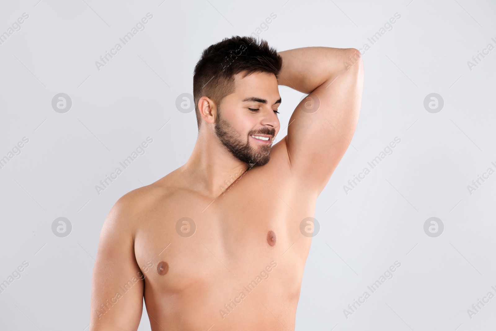 Photo of Young man showing hairless armpit after epilation procedure on light grey background