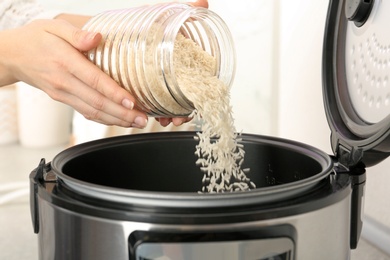 Photo of Woman pouring rice from jar into cooker in kitchen, closeup