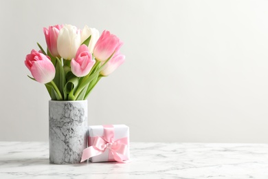 Photo of Bouquet of beautiful spring tulips in vase and gift box on marble table against light background. International Women's Day