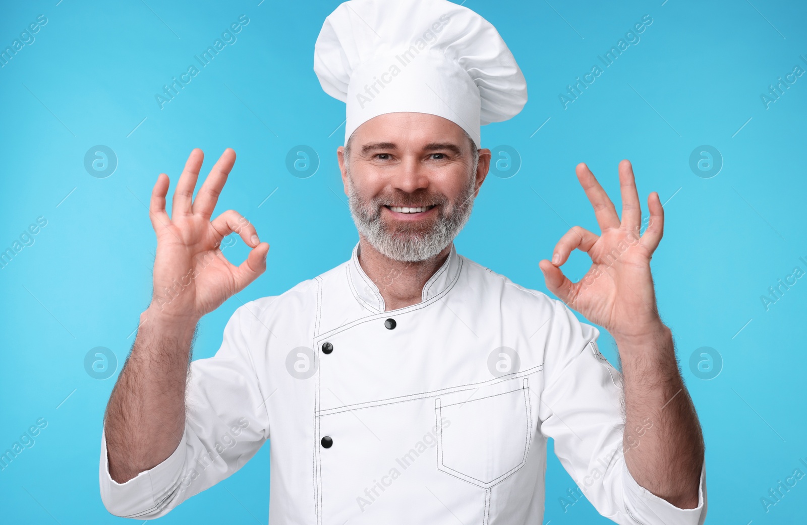 Photo of Happy chef in uniform showing OK gesture on light blue background
