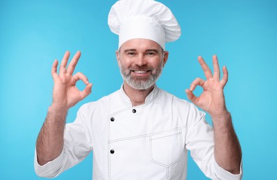 Happy chef in uniform showing OK gesture on light blue background