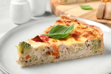 Photo of Tasty quiche with chicken, vegetables, basil and cheese on light table, closeup