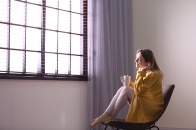 Photo of Young woman relaxing near window with blinds at home. Space for text