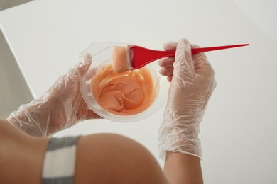 Woman preparing hair dye in bowl at white table, closeup