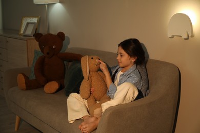 Little girl with toy bunny in living room lit by night lamp