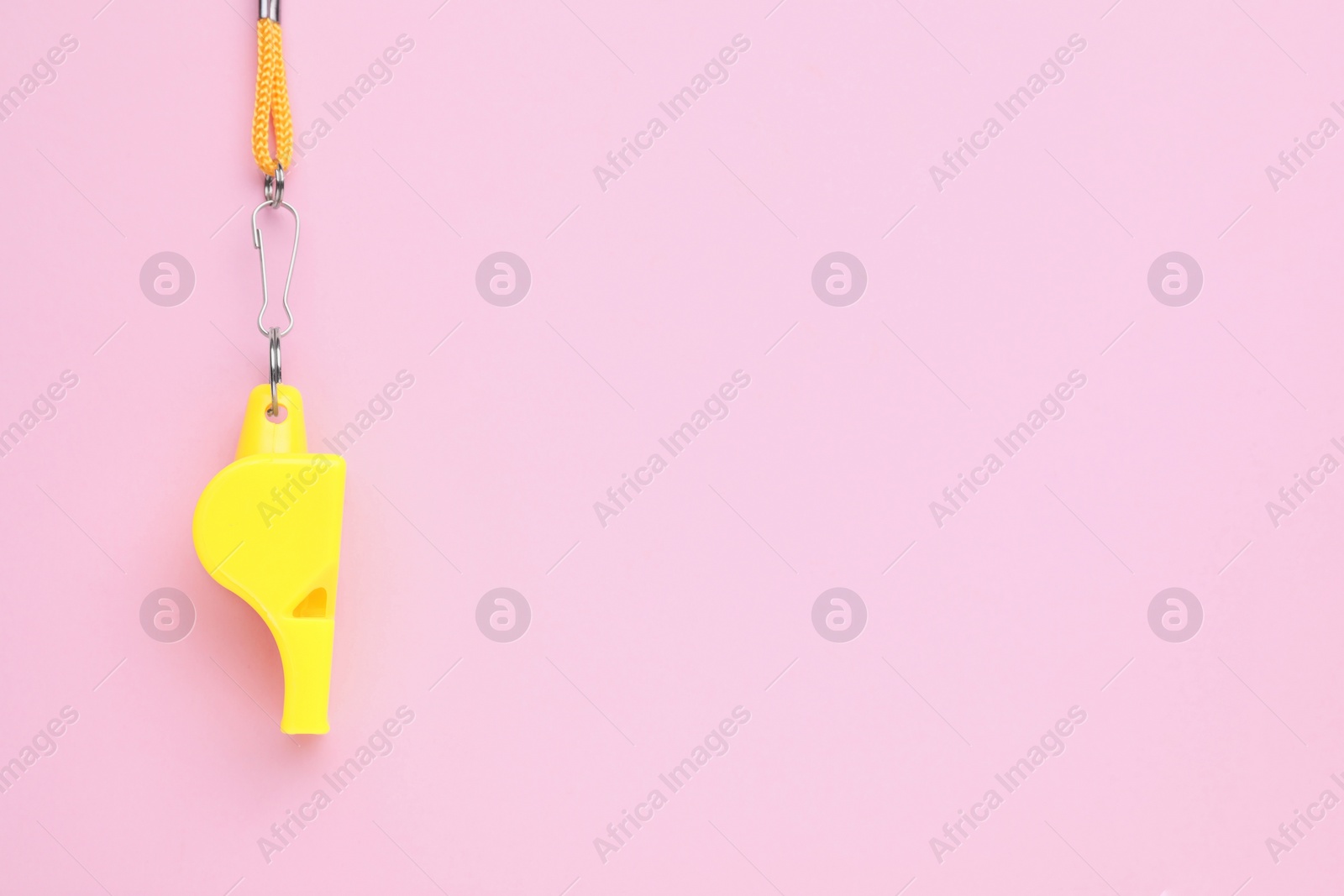 Photo of One yellow whistle with orange cord on pink background, top view. Space for text