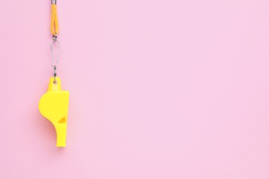 One yellow whistle with orange cord on pink background, top view. Space for text