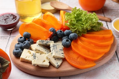 Delicious persimmon, blue cheese and blueberries on tiled surface, closeup
