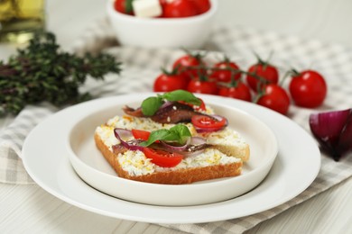 Photo of Delicious sandwiches with anchovies, tomato, onion and basil on white wooden table, closeup