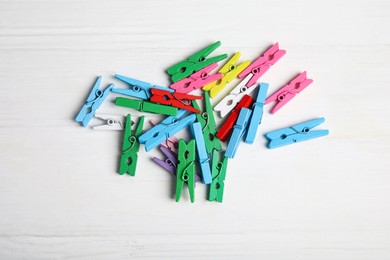 Photo of Pile of colorful clothespins on white wooden table, flat lay