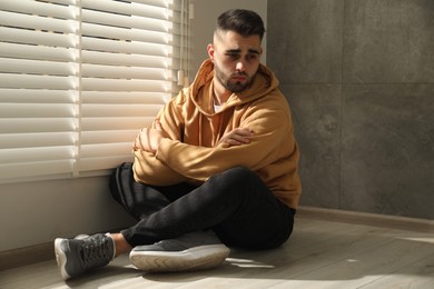 Sad man sitting on floor near window