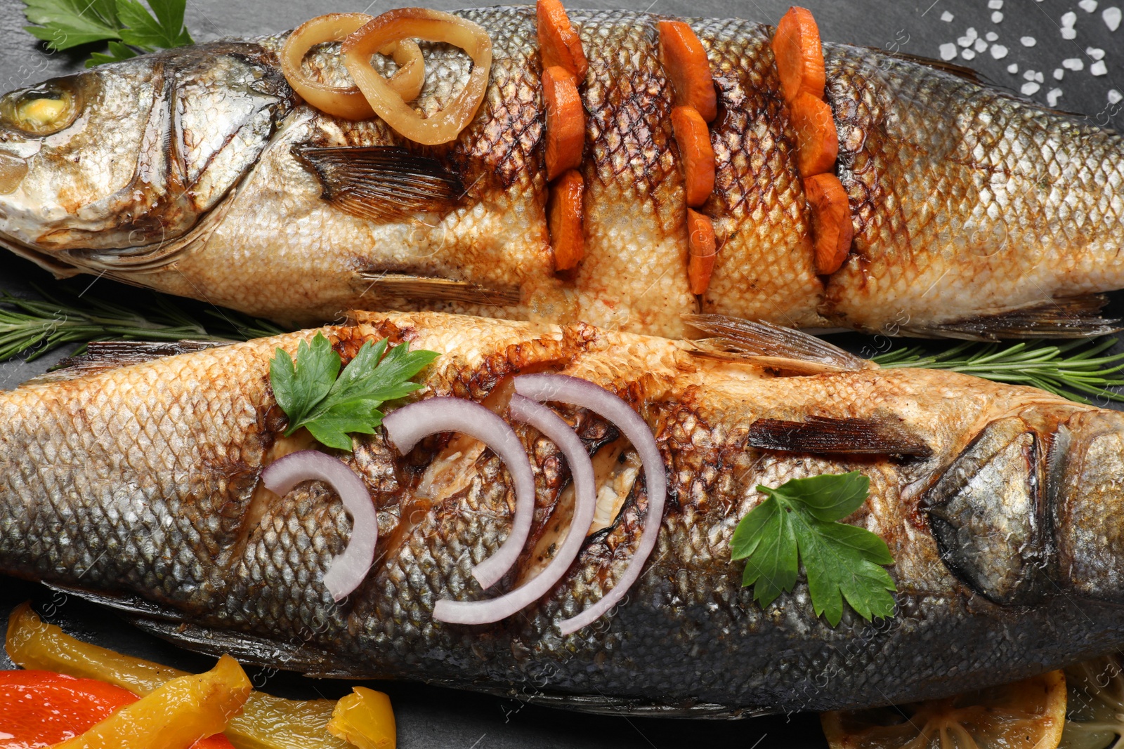 Photo of Delicious baked sea bass fish and ingredients on black plate, closeup