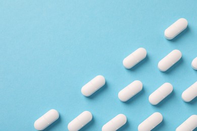 Photo of White pills on light blue background, flat lay. Space for text