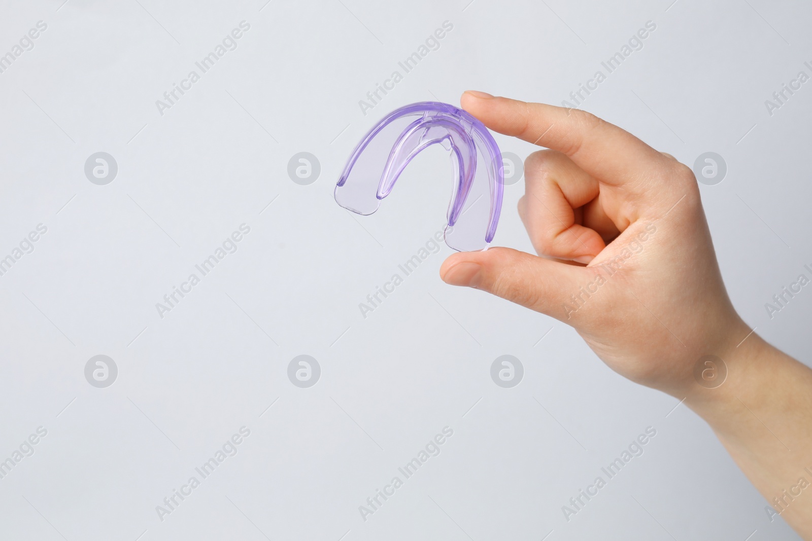 Photo of Woman holding mouth guard on light background, closeup with space for text. Bite correction