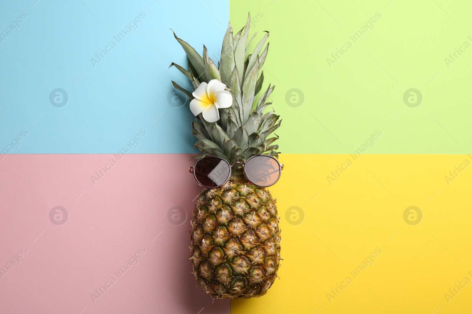 Photo of Pineapple with sunglasses and flower on color background, top view. Creative concept