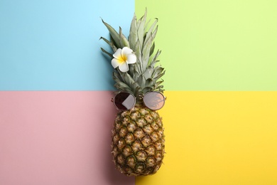 Photo of Pineapple with sunglasses and flower on color background, top view. Creative concept