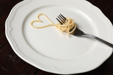 Photo of Heart made of tasty spaghetti and fork on wooden table