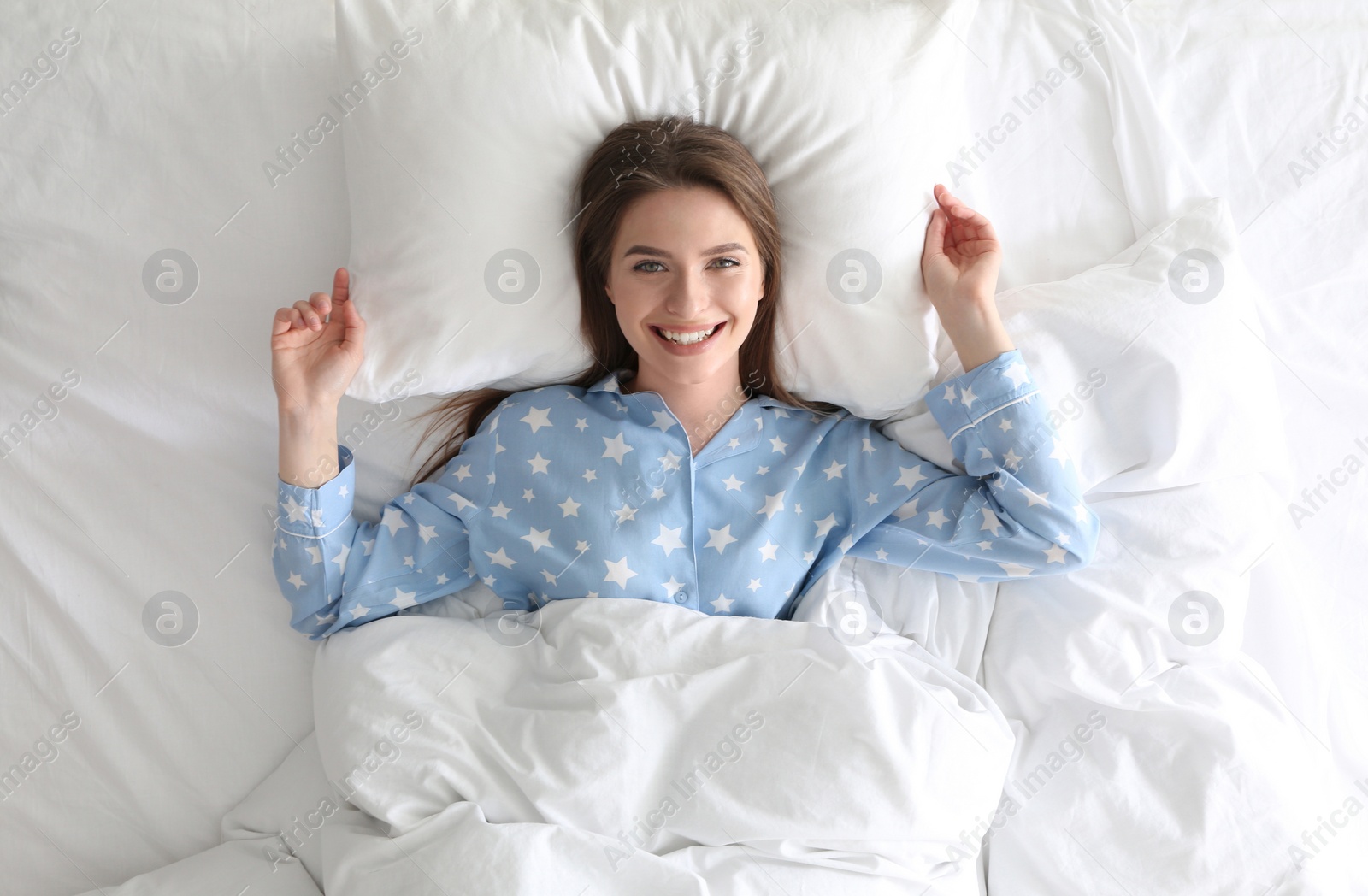 Photo of Young woman lying on comfortable pillow in bed at home, top view