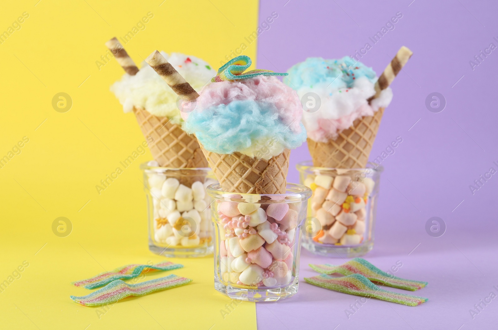 Photo of Sweet cotton candies in waffle cones and marshmallows on color background, closeup