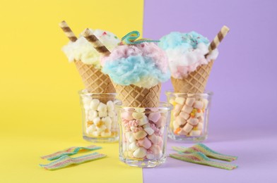 Photo of Sweet cotton candies in waffle cones and marshmallows on color background, closeup