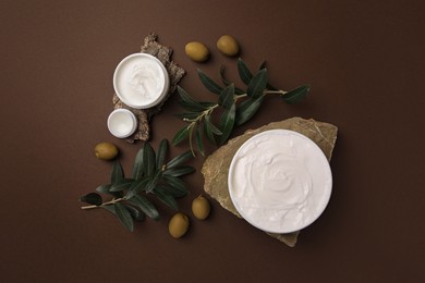 Flat lay composition with jars of cream and olives on brown background