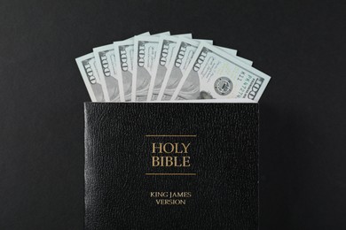 Photo of Holy Bible with money on black background, top view