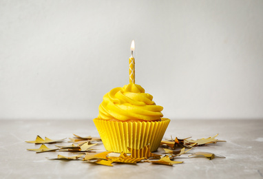 Photo of Delicious birthday cupcake with cream and burning candle on table