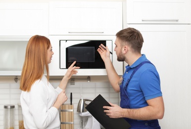 Housewife and repairman near microwave oven in kitchen