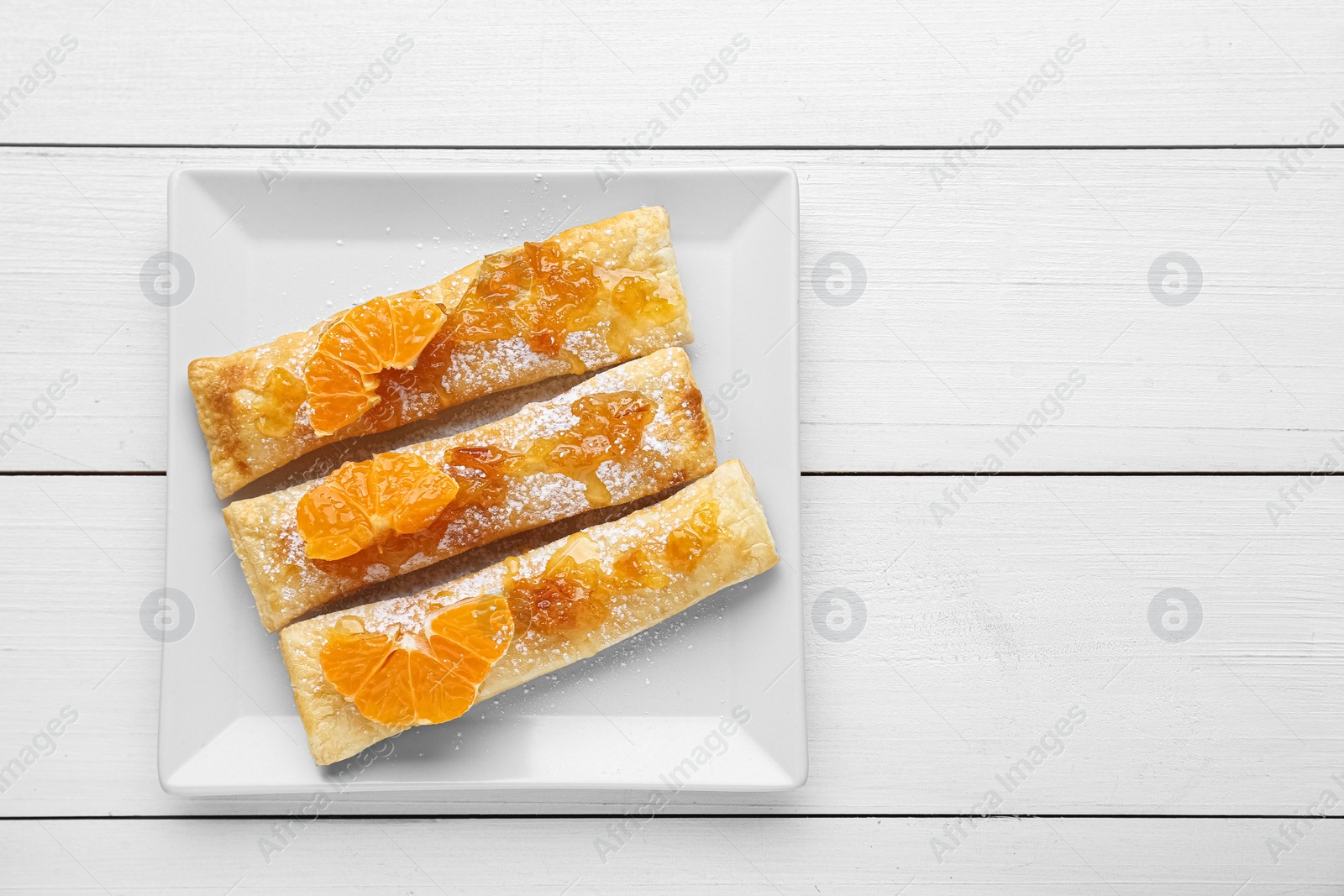 Photo of Fresh tasty puff pastry with sugar powder and tangerines on white wooden table, top view. Space for text