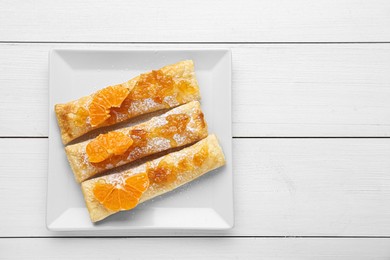 Fresh tasty puff pastry with sugar powder and tangerines on white wooden table, top view. Space for text