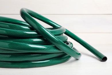 Photo of Green garden hose on white wooden table