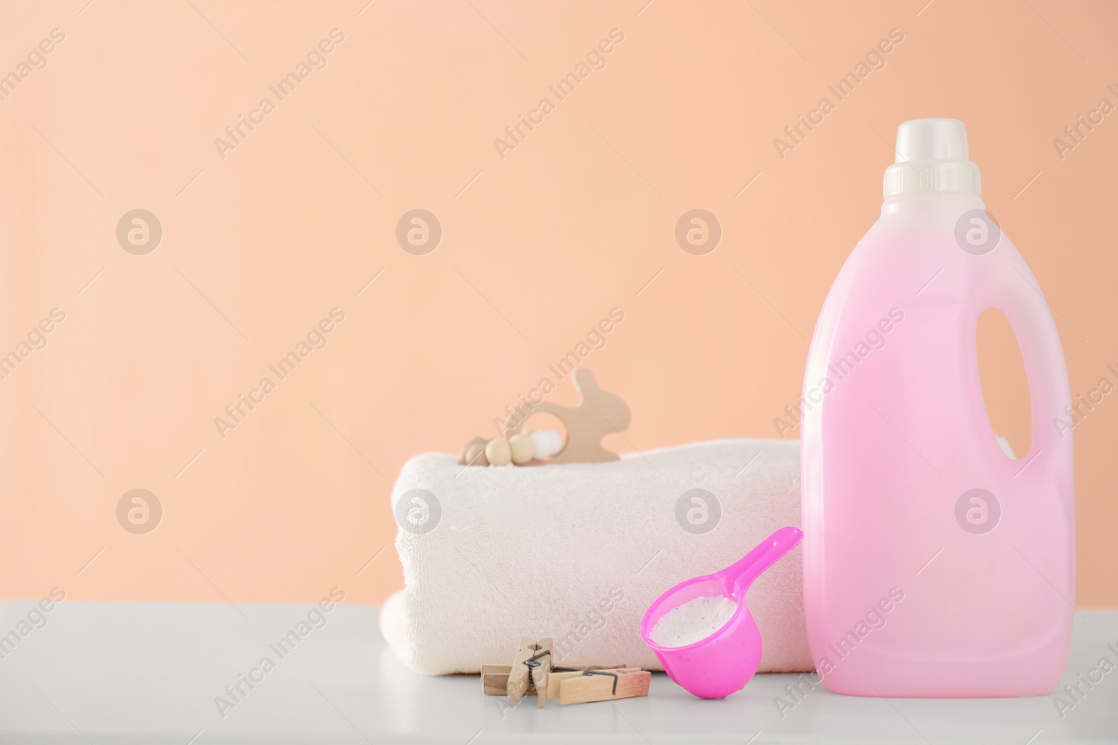 Photo of Detergent and folded towel on white table near pink wall. Space for text