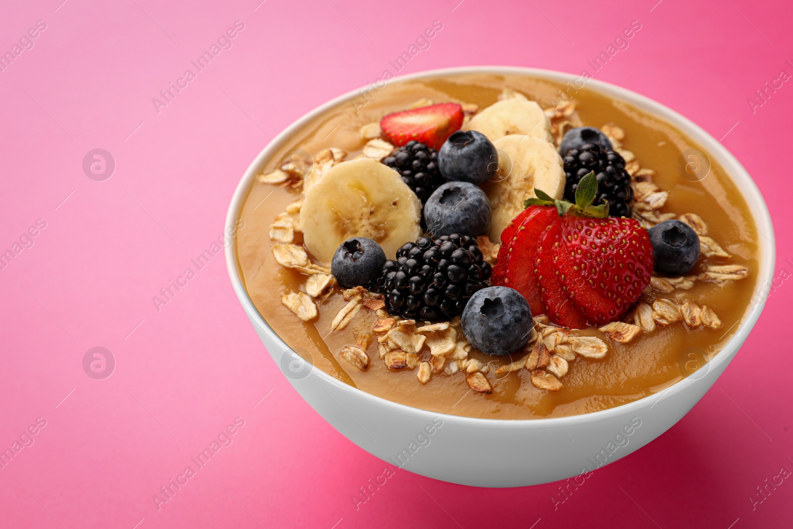 Photo of Delicious smoothie bowl with fresh berries, banana and oatmeal on pink background, closeup