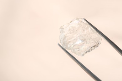 Photo of Tweezers with shiny rough diamond on beige background, closeup