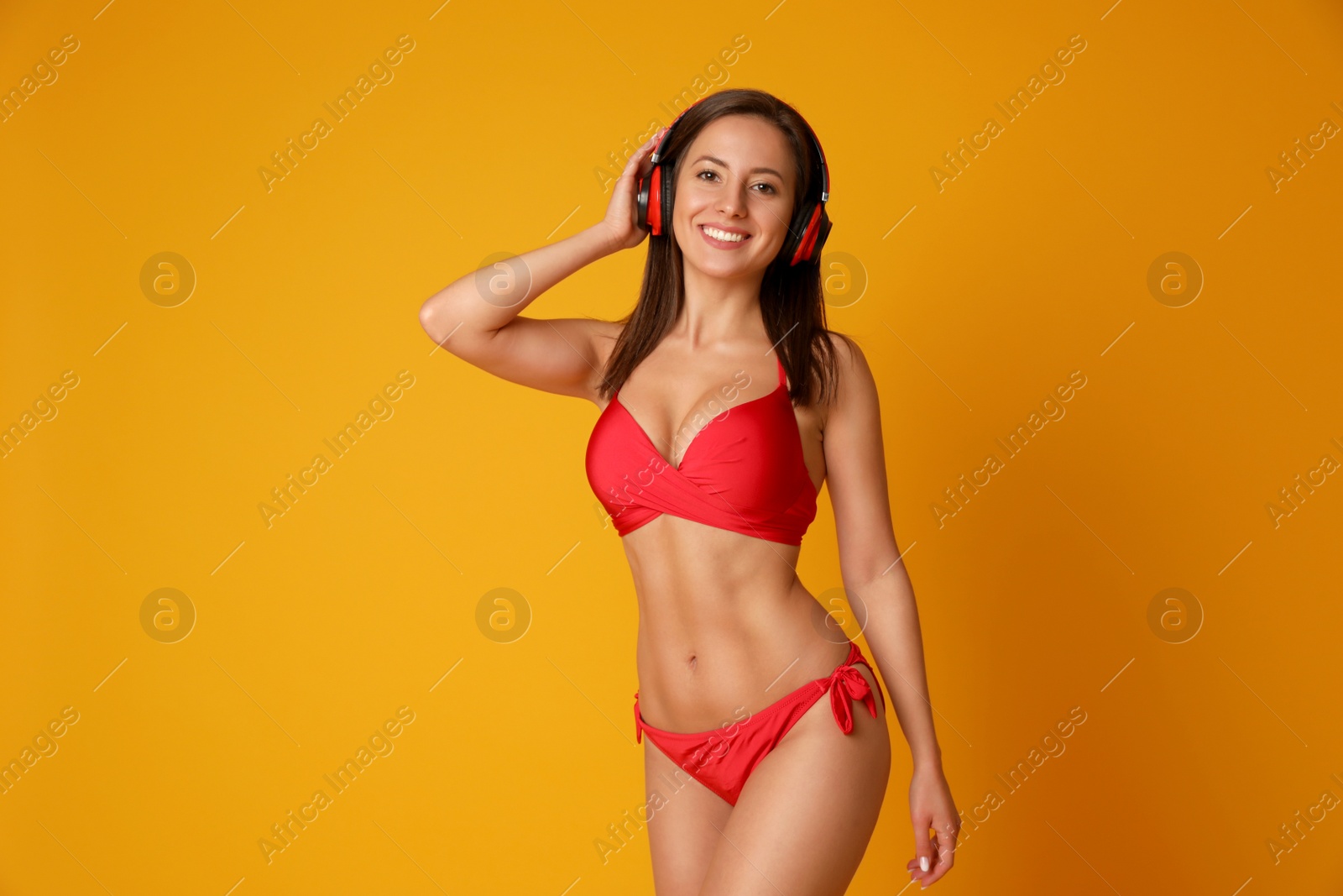 Photo of Pretty sexy woman with slim body in stylish red bikini and headphones on orange background, space for text