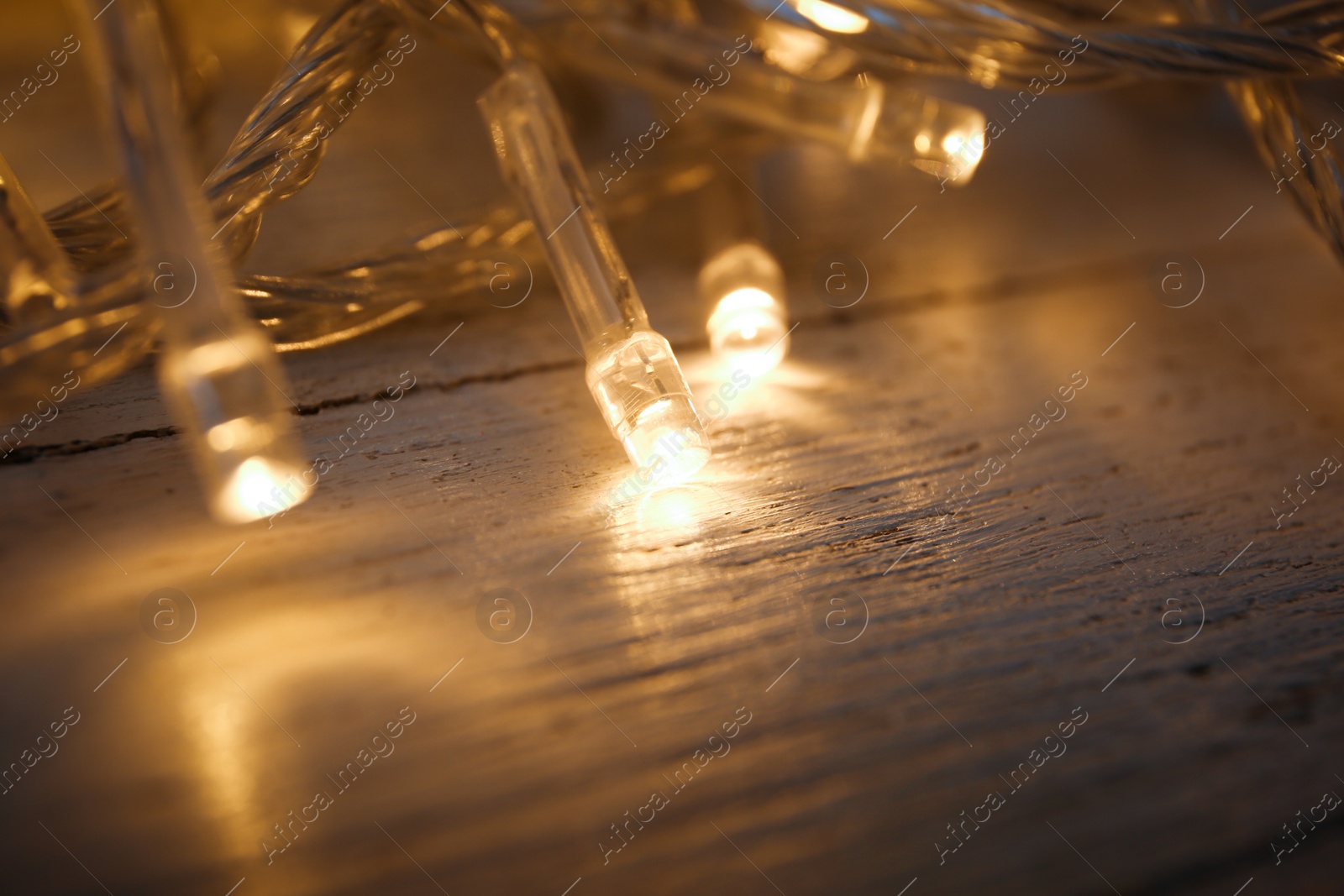 Photo of Glowing Christmas lights on white wooden background, closeup