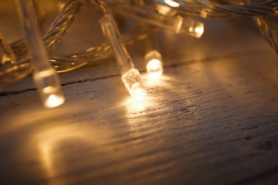 Photo of Glowing Christmas lights on white wooden background, closeup