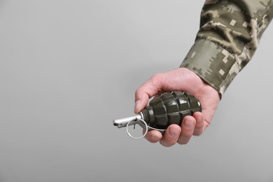 Photo of Soldier holding hand grenade on light grey background, closeup with space for text. Military service