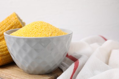 Photo of Raw cornmeal in bowl and corn cobs on table, closeup. Space for text