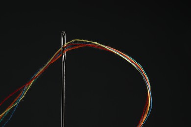 Sewing needle with colorful threads on black background