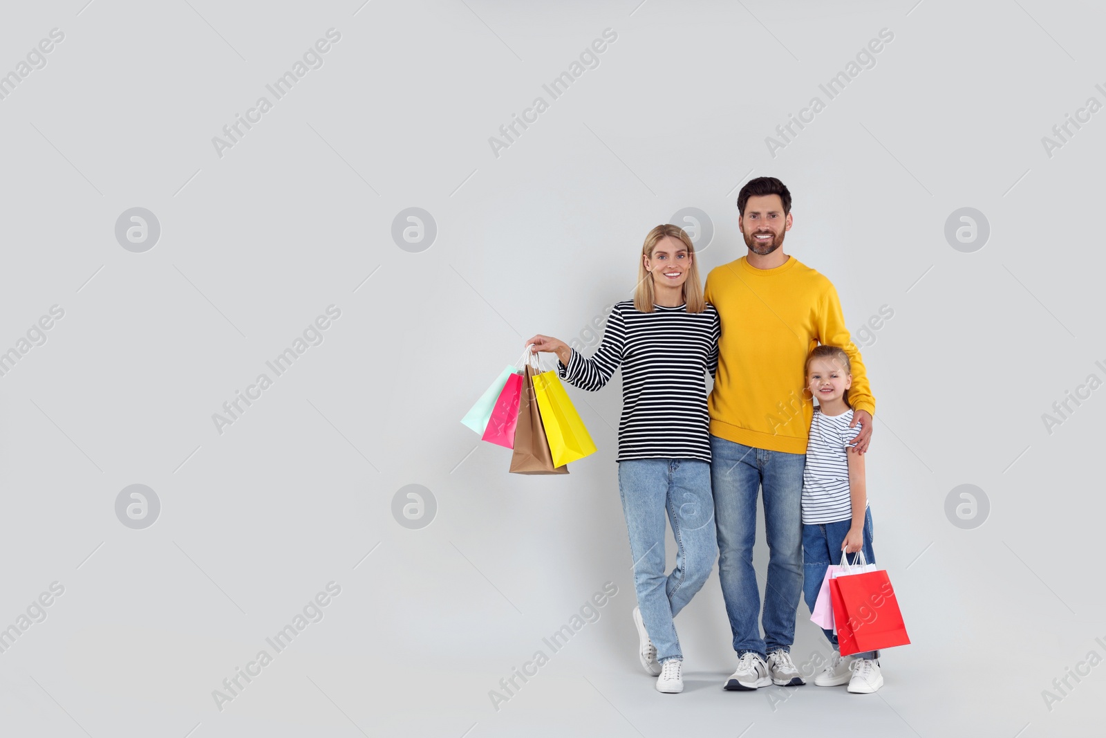 Photo of Family shopping. Happy parents and daughter with many colorful bags on light grey background. Space for text