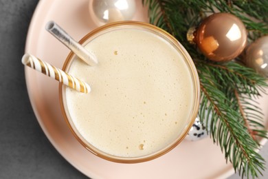Photo of Glass of delicious eggnog and decorated fir branch on gray table, flat lay